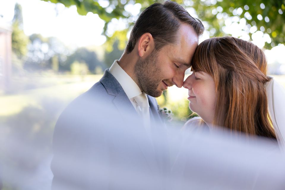 Bruidspaar in intieme kus onder bomen, bruiloft trouwfotografie