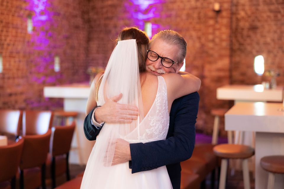Vader omhelst bruid in kerk, emotioneel bruiloft moment trouwfotografie