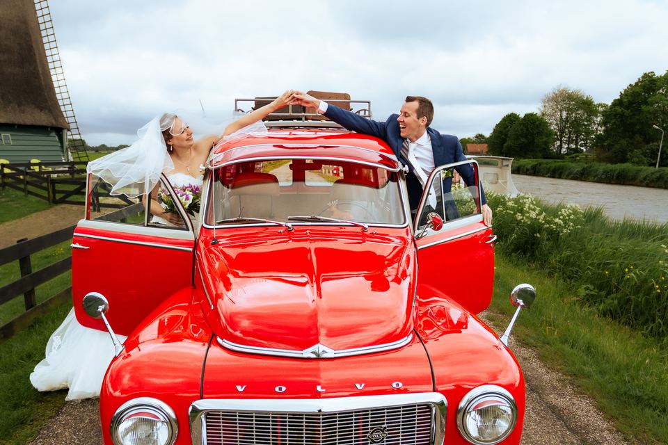 Bruidspaar in rode vintage auto met bloemen, bruiloft trouwauto decoratie