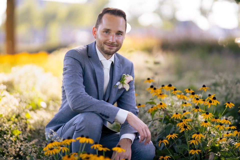Bruidegom met boutonniere zittend in bloemenveld, portret bruiloft