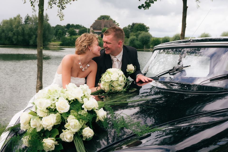 Bruidspaar kijkt elkaar aan met bloemen op auto, bruiloft moment