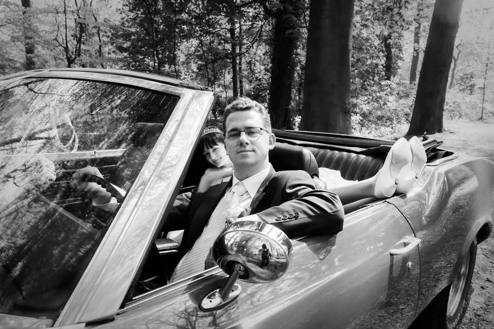 Bruidegom relaxt in open vintage auto omgeven door bos