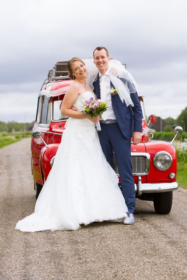 Bruidspaar naast rode vintage auto op landelijke weg