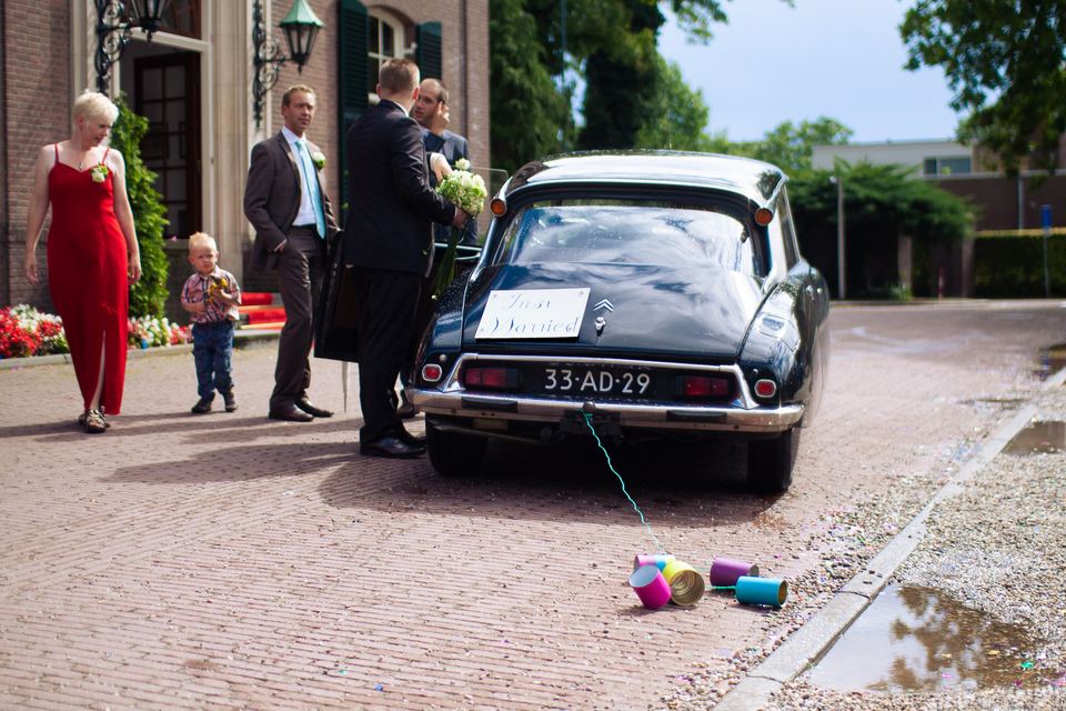 Bruidspaar aankomst met rode vintage auto voor huis