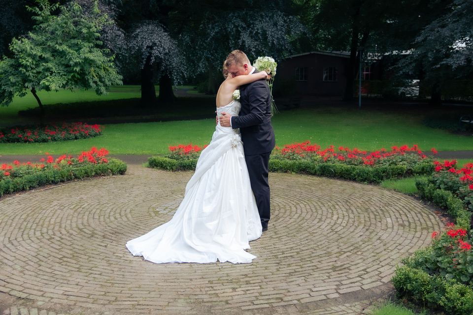 Bruidegom kust bruid op stenen terras omringd door rode bloemen en groen gazon
