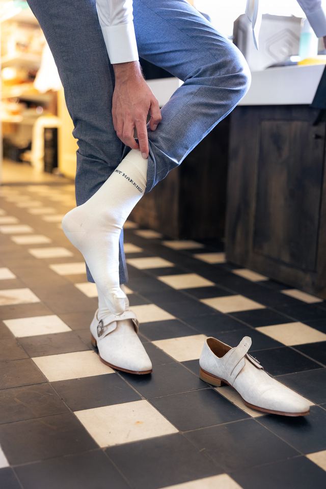 Close-up van groom's witte schoenen en lichte sokken op schaakbordvloer