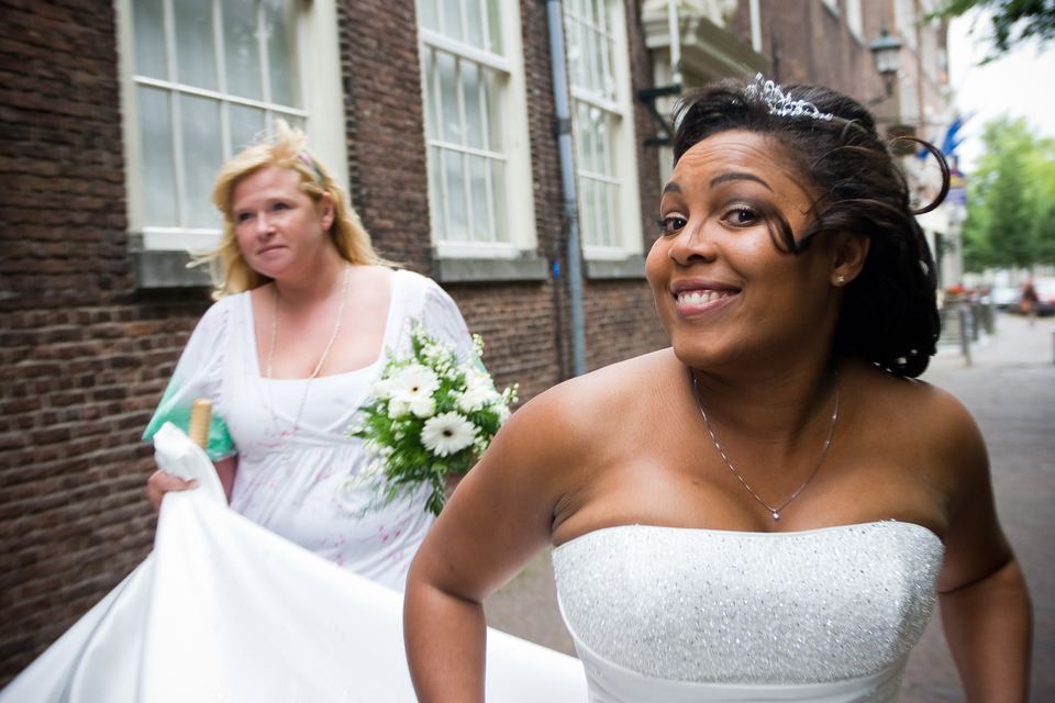 Trouwfoto bruid in witte jurk lachend met bruidsmeisje in roze op straat