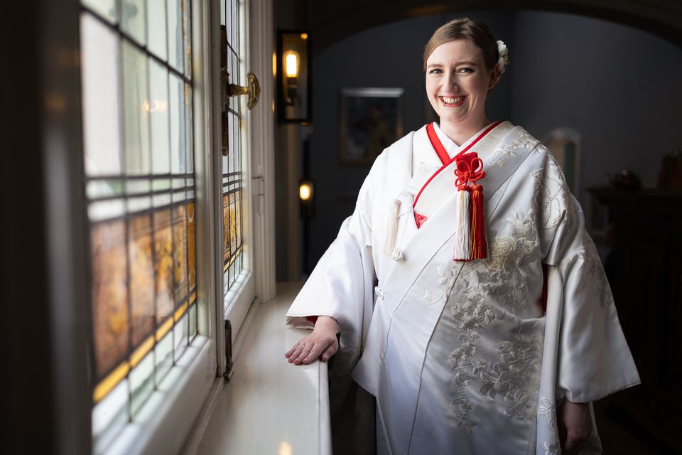 Bruid in witte japanse trouwkimono bij raam, glimlachend